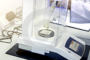 Scientist pipette a sample to sheet PMMA Poly methyl methacrylate acrylic plate on analytical balance to know the exact weight photo