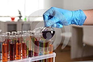 Scientist pouring liquid from retort flask into test tube at laboratory. Solution chemistry