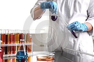 Scientist pouring liquid from retort flask into test tube at laboratory