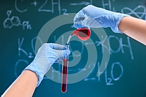 Scientist pouring liquid into test tube against chalkboard. Chemistry glassware