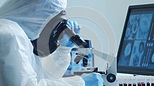 Scientist in protection suit and masks working in research lab using laboratory equipment: microscopes, test tubes