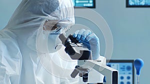 Scientist in protection suit and masks working in research lab using laboratory equipment: microscopes, test tubes