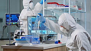 Scientist in protection suit using micropipette filling test tubes photo