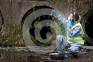 Scientist in protective suit, gloves and mask, holding a vial of liquid and is calling on mobile phone user to report results of