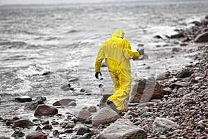 Scientist in protective suit with plastic container walking in on rocky beach