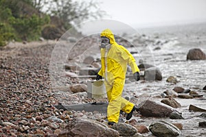 Scientist in protective suit with silver case walking in on rocky beach