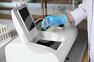 Scientist putting sample compartment with liquid in spectrophotometer. Laboratory analysis