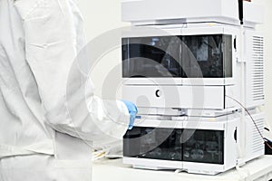 Scientist in rubber gloves and white lab coat standing near high performance liquid chromatography HPLC for separation