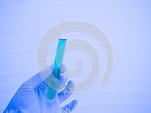 A scientist`s hand in a glove holding a glass test tube with a blue liquid inside