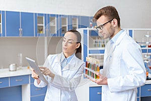 Scientist showing digital tablet to colleague holding test tubes