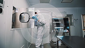 Scientist in sterile clothes takes stack of trays out desinfection chamber