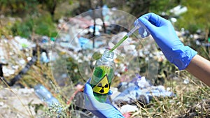 Scientist taking sample from bottle with radiation sign against open dumping