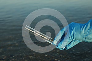 Scientist with test tube taking sample from river for analysis, closeup