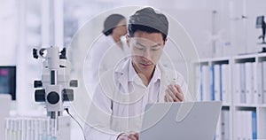 Scientist using a laptop while analyzing test tubes of samples in a lab. Male pathologist doing forensic research while