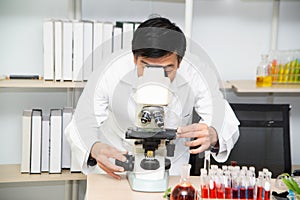 Scientist using Microscope in Laboratory. Male Researcher wearing white Coat sitting at Desk and looking at Samples.