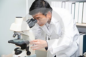 Scientist using Microscope in Laboratory. Male Researcher wearing white Coat sitting at Desk and looking at Samples.
