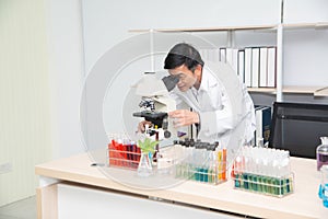 Scientist using Microscope in Laboratory. Male Researcher wearing white Coat sitting at Desk and looking at Samples.