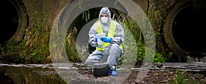 The scientist, wearing a protective suit, gloves and mask, took the liquid from the river, in test tubes, and writes the results