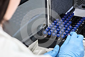 Scientist in a white lab coat putting vial with a sample into autosampler of HPLC system. High performance liquid