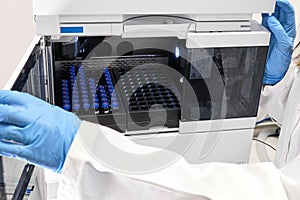 Scientist in a white lab coat putting vial with a sample into autosampler of HPLC system. High performance liquid