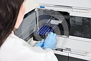 Scientist in a white lab coat putting vial with a sample into autosampler of HPLC system. High performance liquid