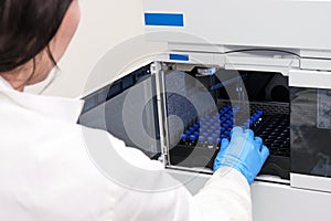 Scientist in a white lab coat putting vial with a sample into autosampler of HPLC system. High performance liquid