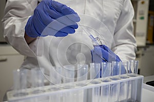 Scientist working in an analytical chemistry laboratory. Gloved hands using a pipette and test tubes to analyse a sample