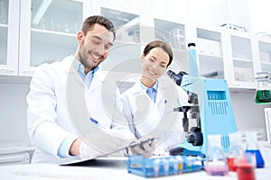 Scientists with clipboard and microscope in lab