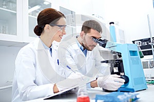 Scientists with clipboard and microscope in lab