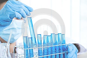 Scientists hand hold a glass tube filled with blue chemical liquid for research and analysis in a laboratory