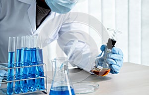 Scientists hold a glass tube filled with orange chemical liquid for research and analysis in a laboratory