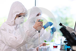 Scientists in protection suits and masks working in research lab using laboratory equipment: microscopes, test tubes.