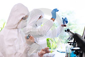 Scientists in protection suits and masks working in research lab using laboratory equipment: microscopes, test tubes.