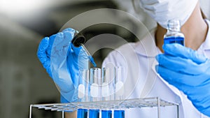 Scientists researching in laboratory in white lab coat, gloves analysing, looking at test tubes sample, biotechnology concept