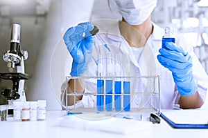 Scientists researching in laboratory in white lab coat, gloves analysing, looking at test tubes sample, biotechnology concept