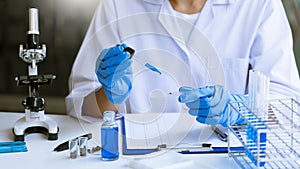 Scientists researching in laboratory in white lab coat, gloves analysing, looking at test tubes sample, biotechnology concept
