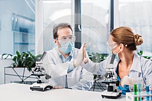 scientists in white coats medical masks and goggles giving high five to each other