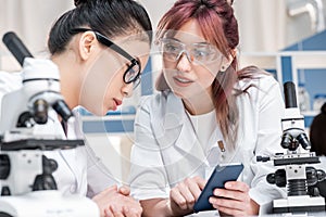 Scientists working together with microscopes and smartphone in chemical lab