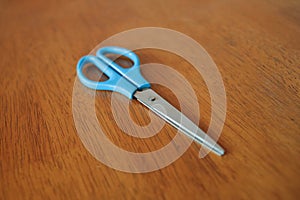 Scissor with blue handle on wooden table background