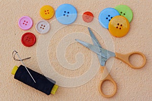 Scissor, buttons, needle, thread on peach colour cloth