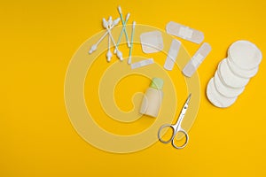 Scissors, adhesive tape, cotton swabs and pads on a yellow background