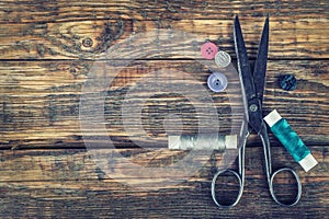 Scissors, bobbins with thread and needles. Old sewing tools on the old wooden background.