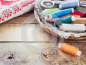 Scissors, bobbins with thread and needles, striped fabric. Old sewing tools on the old wooden background.