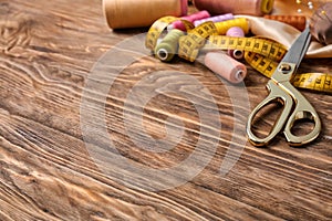 Scissors with color threads and measuring tape on wooden background