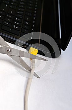 Scissors cut the cable connected to a laptop