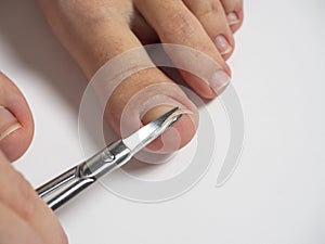 Scissors cut the nails on the big toe of a woman`s foot. The concept of the care of nails and feet