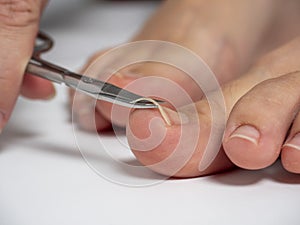 Scissors cut the nails on the big toe of a woman`s foot. The concept of the care of nails and feet. selective focus