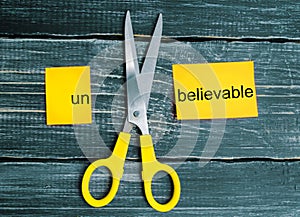 Scissors cut the word unbelievable. concept believable. cuts the