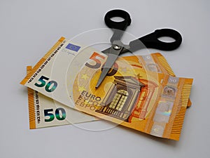 A scissors cuts some banknotes