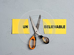 Scissors Cutting off the Word Un of Unbelievable. Concept of possibility, belief, positive thinking, confidence, optimism